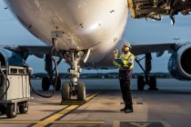 Trabajador de la tripulación de tierra del aeropuerto revisando avión en asfalto - foto de stock