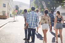 Amis adolescents avec planches à roulettes marchant sur la rue urbaine ensoleillée — Photo de stock