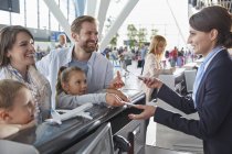 Rappresentante del servizio clienti che aiuta la famiglia a effettuare il check-in con i biglietti al banco del check-in in aeroporto — Foto stock