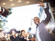 Waving celebrity being interviewed and photographed by paparazzi at event — Stock Photo