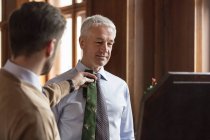 Schneiderin zeigt Krawatte zu Geschäftsmann im Spiegel eines Herrengeschäfts — Stockfoto