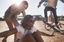 Verspieltes Teenager-Mädchen schubst Freundin auf Skateboard im sonnigen Skatepark — Stockfoto