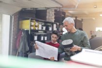 Père et fils avec des plans et une pièce de moteur reconstruire la voiture dans l'atelier de réparation automobile — Photo de stock