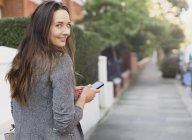 Portrait smiling businesswoman with cell phone looking back on sidewalk — Stock Photo