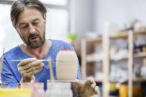 Фокусований зрілий чоловік малює керамічну вазу в студії — стокове фото