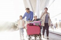 Familia con carrito de equipaje caminando fuera del aeropuerto - foto de stock