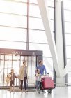Семья прибывает толкая багажную тележку в зале ожидания аэропорта — стоковое фото
