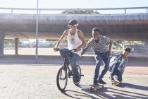 Teenage boys riding BMX bicycle and skateboarding at sunny skate park — Stock Photo