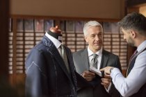 Sastre explicando traje a hombre de negocios en la tienda de ropa masculina - foto de stock
