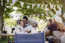 Boyfriend kissing girlfriend with birthday gift at garden party table — Stock Photo