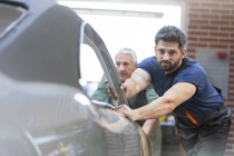 Mecánicos empujando coche en taller de reparación de automóviles - foto de stock