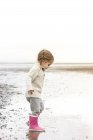 Girl in pink rain boots playing in water on beach — Stock Photo