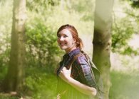 Smiling woman with backpack hiking in sunny woods — Stock Photo