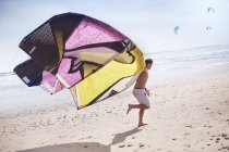 Homme courant avec kiteboarding cerf-volant sur la plage ensoleillée — Photo de stock