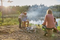 Großeltern und Enkel umarmen sich am Lagerfeuer am sonnigen Seeufer — Stockfoto