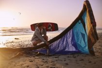 Homme avec équipement de kitesurf sur la plage du coucher du soleil — Photo de stock