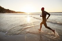Чоловічий тріатлоніст плаває в мокрій костюмі, бігаючи в океанський серфінг на сході сонця — стокове фото