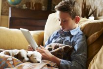 Хлопчик використовує цифровий планшет з цуценятами на колінах вдома — стокове фото