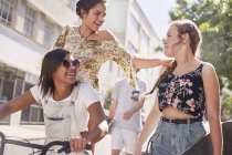 Teenage girls with BMX bicycle and skateboard on sunny urban street — Stock Photo