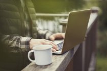 Mann benutzte Laptop und trank Kaffee an Balkongeländer — Stockfoto
