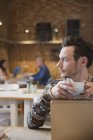Мужчина смотрит в сторону и пьет кофе за ноутбуком в кафе — стоковое фото