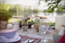 Coloque los ajustes y el ramo simple en la mesa de fiesta del jardín a orillas del lago - foto de stock