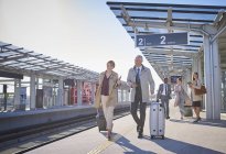 Business people walking pulling suitcases on sunny train station platform — Stock Photo