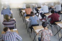 Estudiantes universitarios haciendo exámenes en escritorios en el aula - foto de stock