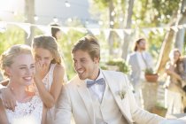 Подружка невесты шепчет невесте на ухо во время свадебного приема в домашнем саду — стоковое фото