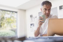 Hombre beber café y trabajar en el ordenador portátil en la cocina - foto de stock