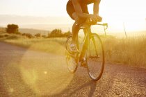 Male cyclist riding bike on sunny sunrise rural road — Stock Photo