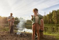 Grandparents and grandchildren cooking at lakeside in woods — Stock Photo