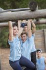 Smiling woman crossing monkey bars on boot camp obstacle course — Stock Photo