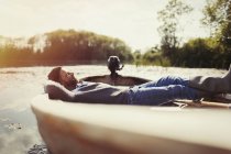 Uomo sereno posa rilassante in canoa sul lago soleggiato — Foto stock