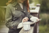 Женщина пьет кофе с помощью цифрового планшета на балконе перила — стоковое фото