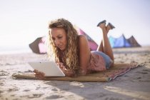 Mujer leyendo tableta digital en alfombra de playa - foto de stock