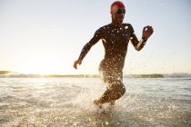 Male triathlete swimmer in wet suit running from ocean — Stock Photo