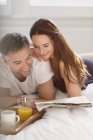 Paar liest gemeinsam Zeitung im Bett — Stockfoto