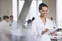 Retrato sonriente estudiante universitaria tomando notas en el aula de laboratorio de ciencias - foto de stock