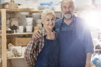 Портрет улыбающейся пожилой пары в фартуках в мастерской керамики — стоковое фото
