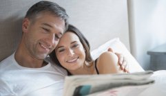 Sorridente coppia lettura giornale a letto — Foto stock