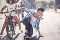 Retrato sorrindo adolescente skate com amigos na ensolarada rua urbana — Fotografia de Stock