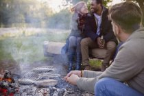 Friends cooking fish in grill basket over campfire — Stock Photo
