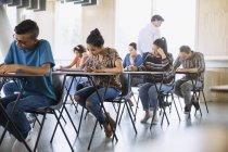 Professor assistindo estudantes universitários fazendo teste em sala de aula — Fotografia de Stock