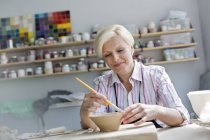 Улыбающаяся взрослая женщина рисует глиняную чашу в студии — стоковое фото