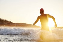 Male triathlete swimmer in wet suit running out of sunny ocean — Stock Photo