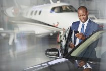 Бізнесмен з мобільним телефоном потрапляє в машину біля корпоративного реактивного літака в ангарі — стокове фото