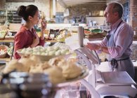 Deli worker offering cheese sample to woman in market — Stock Photo