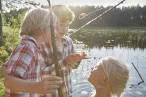 Brothers and sister fishing at sunny pond — Stock Photo