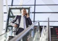 Businessman talking on cell phone on airport escalator — Stock Photo